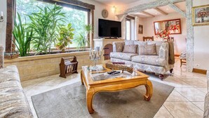 Una sala de estar con un sofá, una mesa de centro, un televisor y una ventana con plantas.