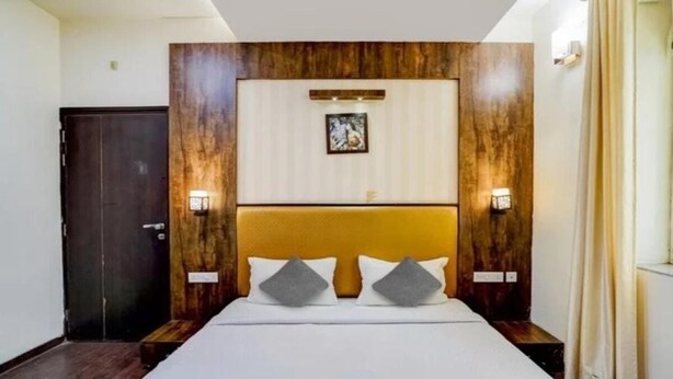 Habitación de hotel con una cama grande, cabecero de madera, dos lámparas de noche y un cuadro en la pared.