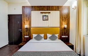 A hotel room with a large bed, wooden headboard, two bedside lamps, and a framed picture on the wall. - Hotel MNG The Platinum (Kanpur)