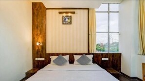 Habitación de hotel con una cama grande, cabecera de madera, un cuadro en la pared y una ventana con cortinas.