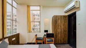 Habitación de hotel con cama, dos sillas, escritorio, ventana con cortinas, aire acondicionado y armario.