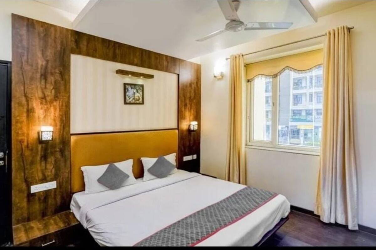 Una habitación de hotel con una cama, ventilador de techo, ventana con cortinas e iluminación montada en la pared.