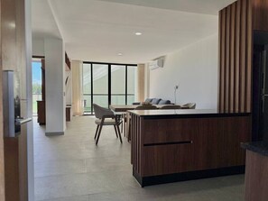 A modern kitchen with a wooden island, a dining area with chairs, and a large window providing natural light. - In the Marina, With Pool and Nice Amenities (Mazatlán)