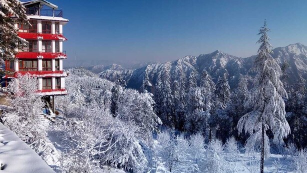 A multi-story building with a red and white facade, surrounded by snow-covered trees and mountains in the background. - Mashobra Heights Hotel by Shalidrishya (Shimla)