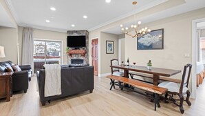 A spacious living room with a fireplace, a dining area with a wooden table and benches, and a large window offering a view of a snowy landscape. - Ski-In Ski-Out Home + Hot Tub + Resort Amenities + Alpine Views | Highline Lodge (Park City)