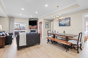 A spacious living room with a fireplace, a dining area with a wooden table and benches, and a large window offering a view of a snowy landscape. - Ski-In Ski-Out Home + Hot Tub + Resort Amenities + Alpine Views | Highline Lodge (Park City)