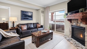 A living room with a fireplace, a sofa, a coffee table, and a TV. - Ski-In Ski-Out Home + Hot Tub + Resort Amenities + Alpine Views | Highline Lodge (Park City)