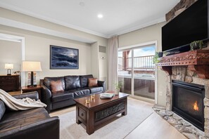 A living room with a fireplace, a sofa, a coffee table, and a TV. - Ski-In Ski-Out Home + Hot Tub + Resort Amenities + Alpine Views | Highline Lodge (Park City)