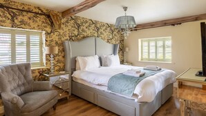 A bedroom with a large bed, a chair, a nightstand, a lamp, and a chandelier. - Wisteria Cottage sleeping 8 (Helmsley)