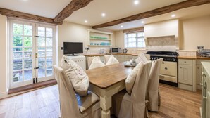 A kitchen with a wooden table and chairs, a stove, a microwave, and a television. - Wisteria Cottage sleeping 8 (Helmsley)