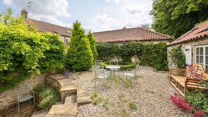 A courtyard with a stone bench, a table with chairs, and a wooden bench with cushions. - Wisteria Cottage sleeping 8 (Helmsley)