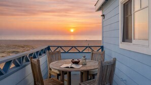 A wooden table with chairs on a balcony overlooking a beach at sunset.