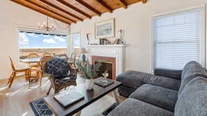A cozy living room with a fireplace, a dining area with wicker furniture, and a large window with blinds.