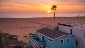 A coastal building with a balcony overlooking a beach at sunset.