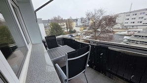Een balkon met een tafel en stoelen, met uitzicht op een parkeerplaats en gebouwen op de achtergrond.