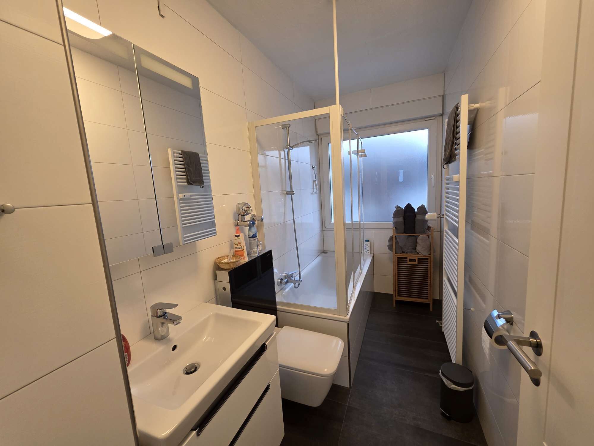 A modern bathroom with a large mirror, a sink, a toilet, and a shower area.