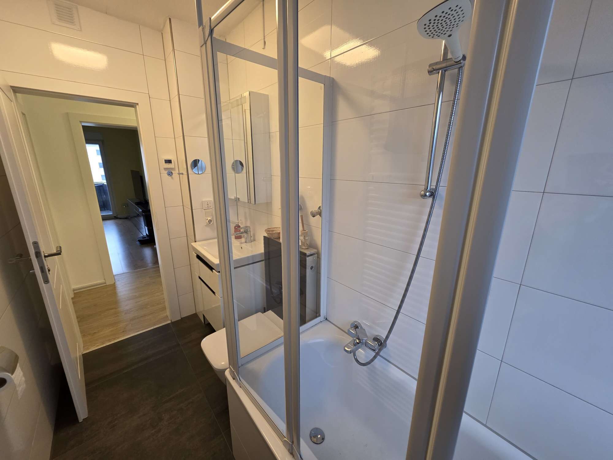 Ett modernt badrum med en dusch som är avskärmad med glasväggar, ett vitt handfat och en spegel.