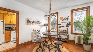 A kitchen with wooden cabinets, a dining table with stools, a chandelier, and a potted plant. - LAST MIN DEAL - Historic Condo - 1 King 2 Queens (Greensboro)
