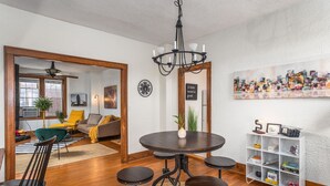 A dining area with a round table, four chairs, a chandelier, and a white shelving unit with various items. - LAST MIN DEAL - Historic Condo - 1 King 2 Queens (Greensboro)