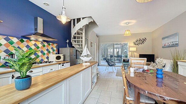 Une cuisine moderne avec un plan de travail en bois, un escalier en colimaçon et un coin repas comprenant une table et des chaises en bois.