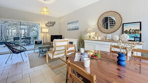 Un vaste espace de vie comprenant une table à manger, des chaises, un téléviseur et une grande fenêtre donnant sur un jardin.