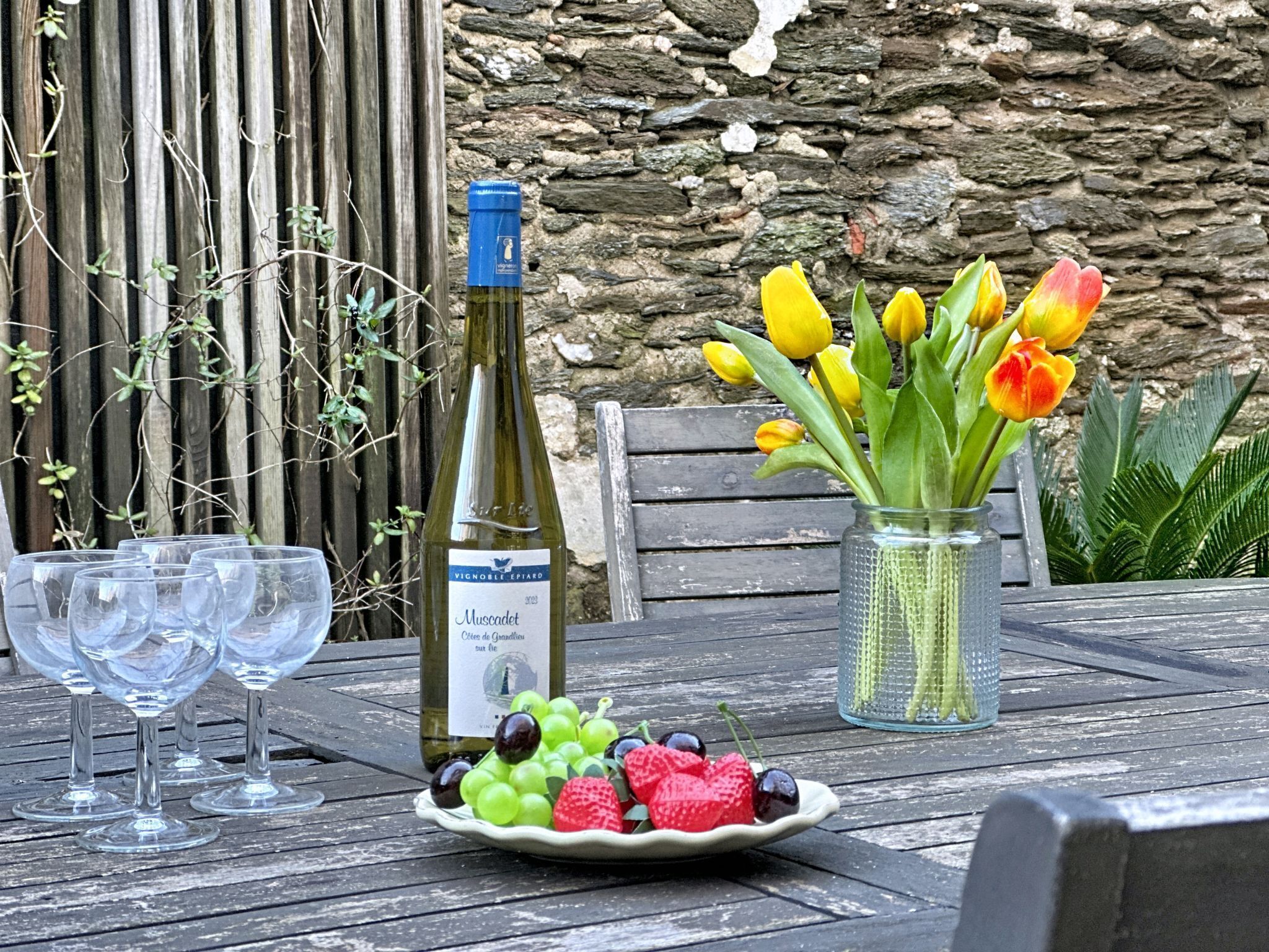 Ett bord med en vinflaska, en tallrik med frukt och en vas med tulpaner.