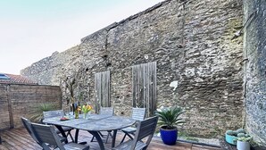Une terrasse en bois avec une table ronde et des chaises, un mur en pierre et des plantes en pot.