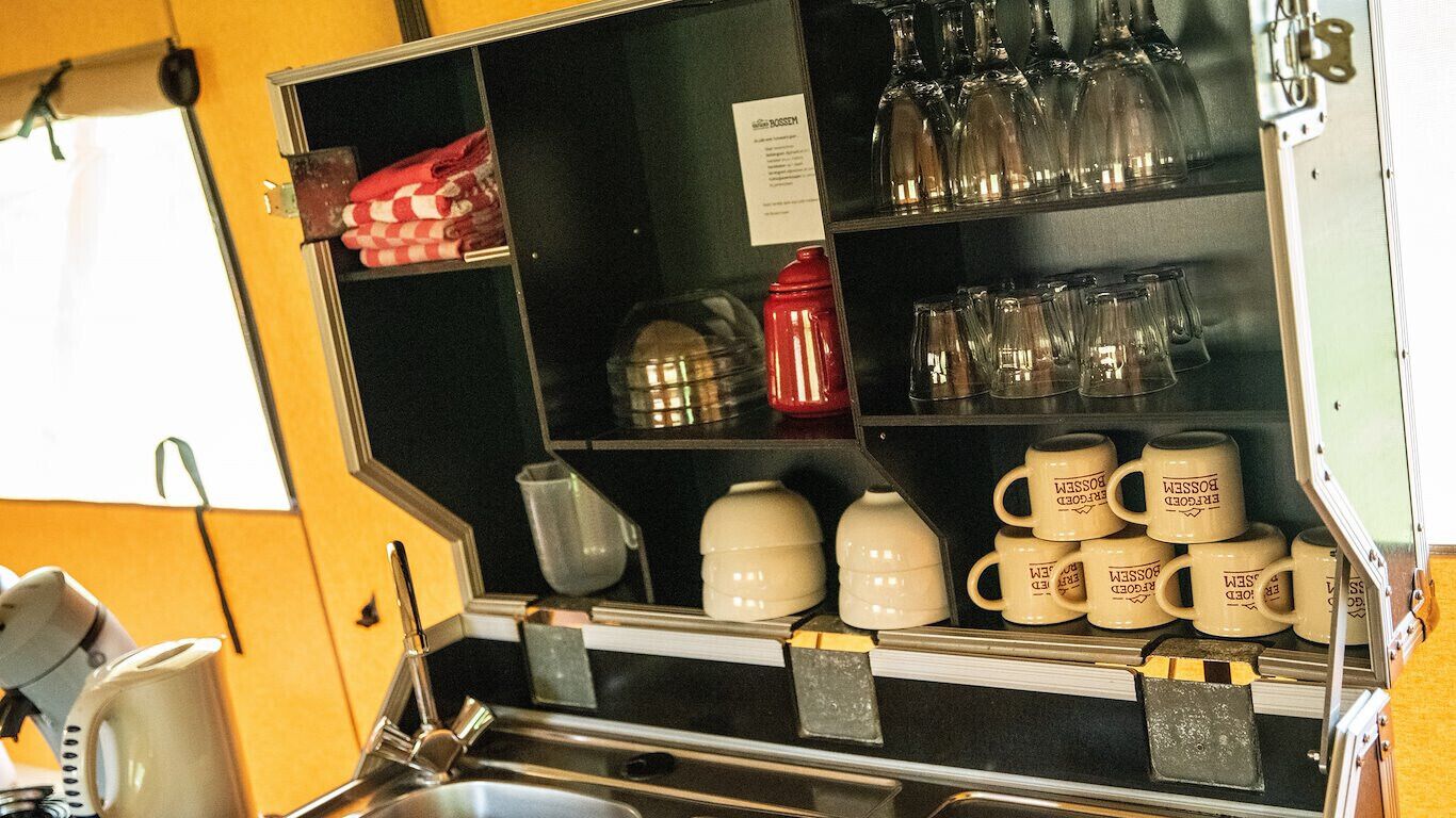 Una zona de cocina con estantes que contienen diversos utensilios de cocina, incluyendo tazas y vasos.