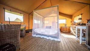 Una habitació amb tenda, un llit sota mosquitera, mobles de vimet, un terra de fusta i una cuinetta.