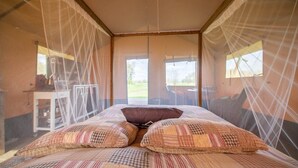 Una habitació amb llit, mosquiteres, una taula amb objectes i vistes a l'exterior.