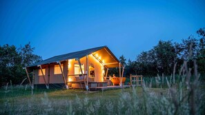 A cozy, well-lit tent-style accommodation with a porch area, surrounded by natural vegetation. - Erfgoed Bossem - Sterrenkubus (Lattrop-Breklenkamp)