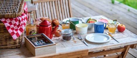A wooden table set with breakfast items including croissants, a red teapot, a glass of juice, and a plate of food.