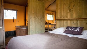 Ein Zimmer in einer Holzhütte mit einem Bett, einem Holzeimer und einem Fenster.
