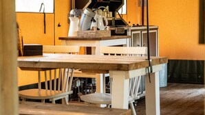 Ein Essbereich mit Holztisch und weißen Stühlen, Küchengeräten auf einer Arbeitsplatte sowie einem Fenster mit Vorhang.