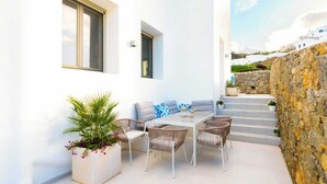 A white building with a patio area featuring a table, chairs, and a sofa. - Eidolion Essence - Mykonos Villa with Private Pool (Mykonos)
