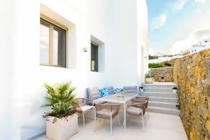 A white building with a patio area featuring a table, chairs, and a sofa. - Eidolion Essence - Mykonos Villa with Private Pool (Mykonos)