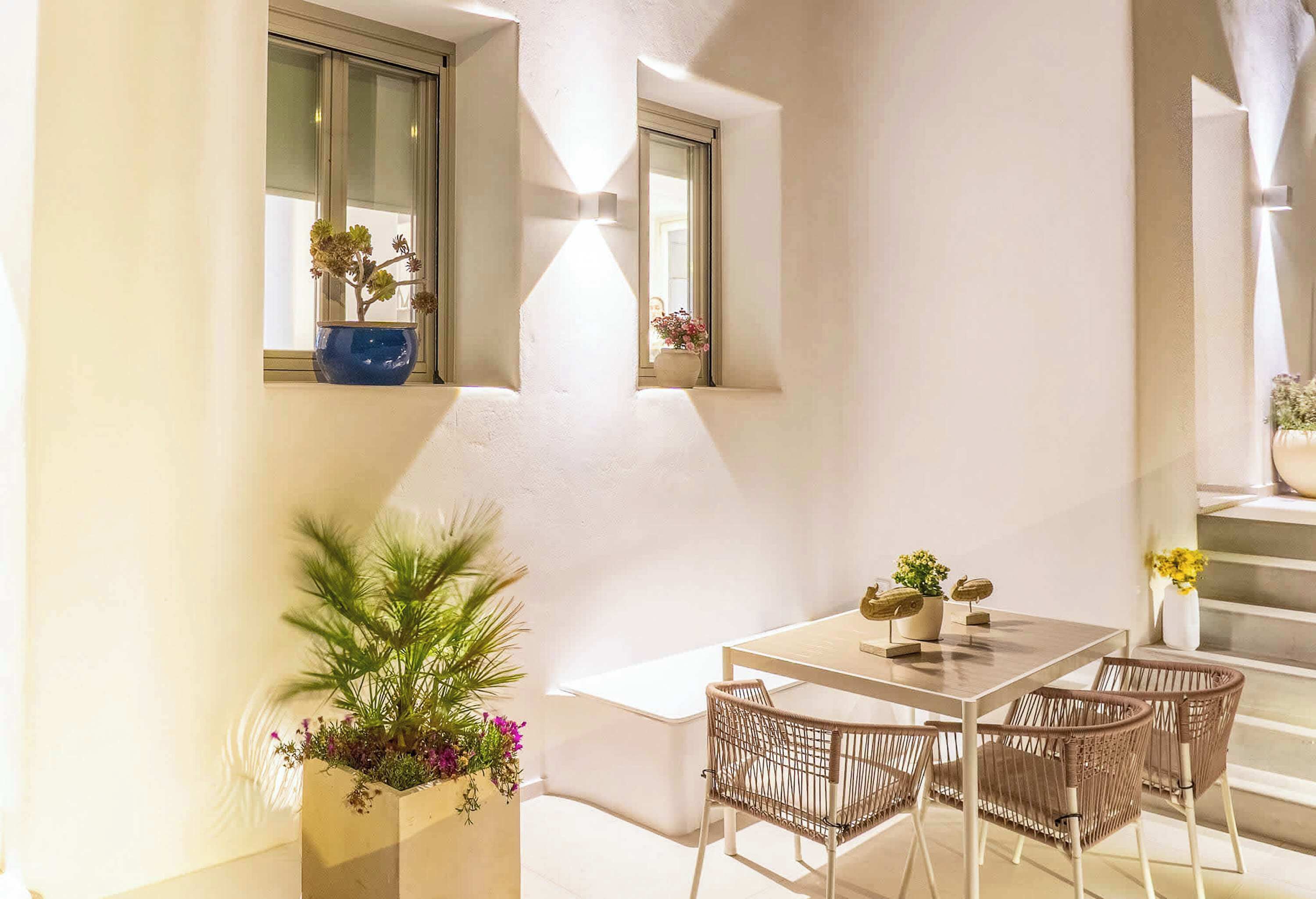 Un patio iluminado por el sol con una mesa y sillas, una planta en maceta y una ventana con vistas.