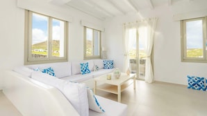 A bright room with a white sofa, a small table, and large windows. - Eidolion Essence - Mykonos Villa with Private Pool (Mykonos)