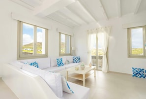 A bright room with a white sofa, a small table, and large windows. - Eidolion Essence - Mykonos Villa with Private Pool (Mykonos)