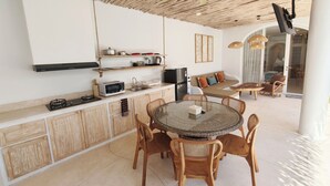A modern kitchen with a gas stove, microwave, and a built-in oven. There is a dining area with a round glass table and wicker chairs. - Melvana Villa Uluwatu (Ungasan)