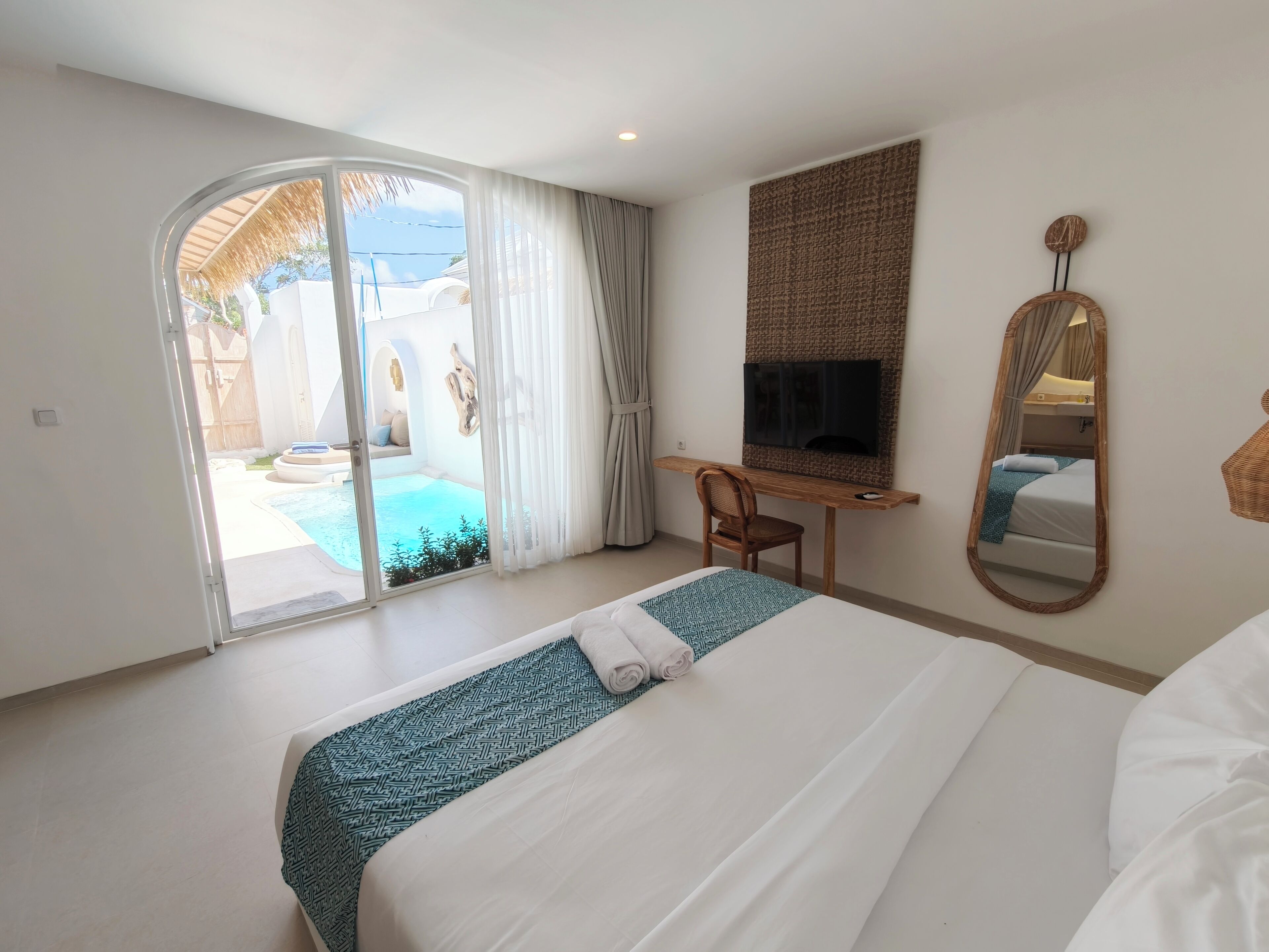Un dormitorio con cama, escritorio, silla, televisor y puerta corrediza a la zona de la piscina.