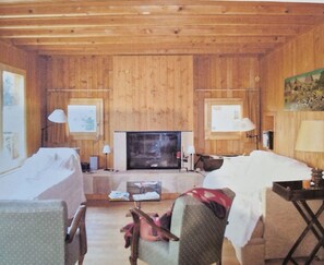 A cozy room with wooden walls, a fireplace, a bed, a desk, and two lamps. - Large traditional chalet with all modern amenities, located 750 meters from the gondola (Ollon)
