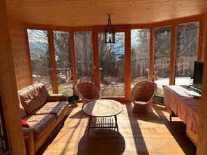 A wooden interior with a sofa, two wicker chairs, a round table, and large windows offering a view of a wooded area. - Large traditional chalet with all modern amenities, located 750 meters from the gondola (Ollon)