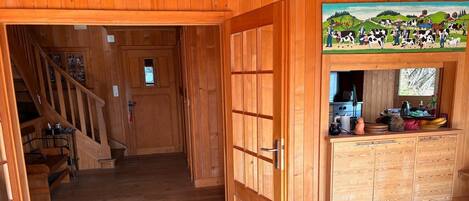 A wooden cabin interior with a wooden staircase, a kitchen area with cabinets, and a painting above the counter.
