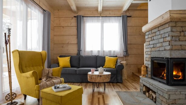 Een gezellige woonkamer met een open haard, een bank, een gele fauteuil en een salontafel.
