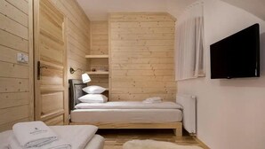 Een knus kamertje met een bed, nachtkastje, lamp en een aan de muur bevestigde televisie.