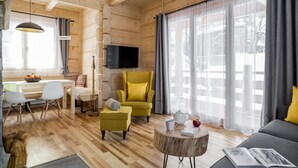 Een knus woongedeelte met houten inrichting, een aan de muur bevestigde televisie en een eethoek met stoelen en een tafel.