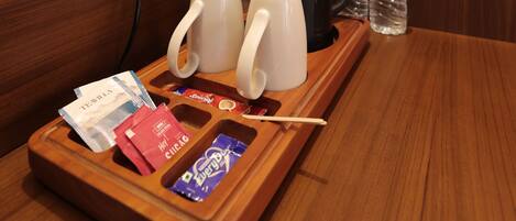 A wooden tray with a coffee maker, two mugs, a bottle of water, and a tray with snacks and a toothbrush.