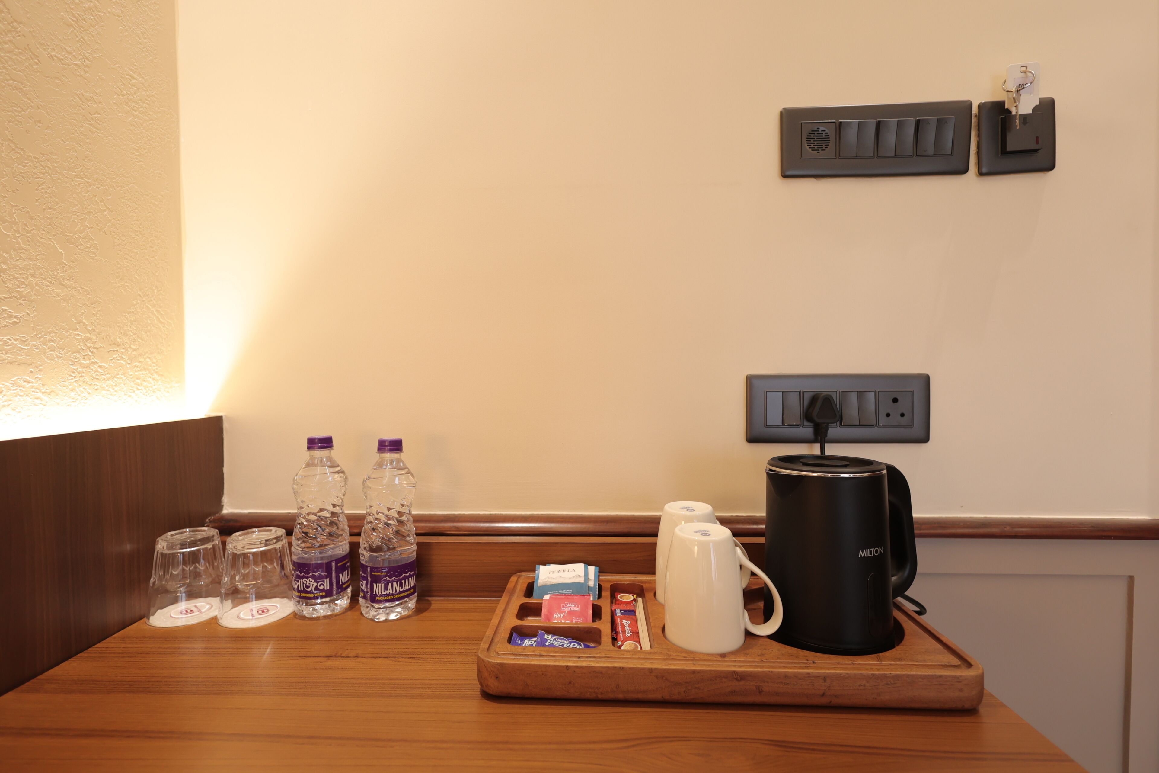 Ett hotellrum med ett träbricka som innehåller en vattenflaska, en kaffebryggare och ett fat med snacks.