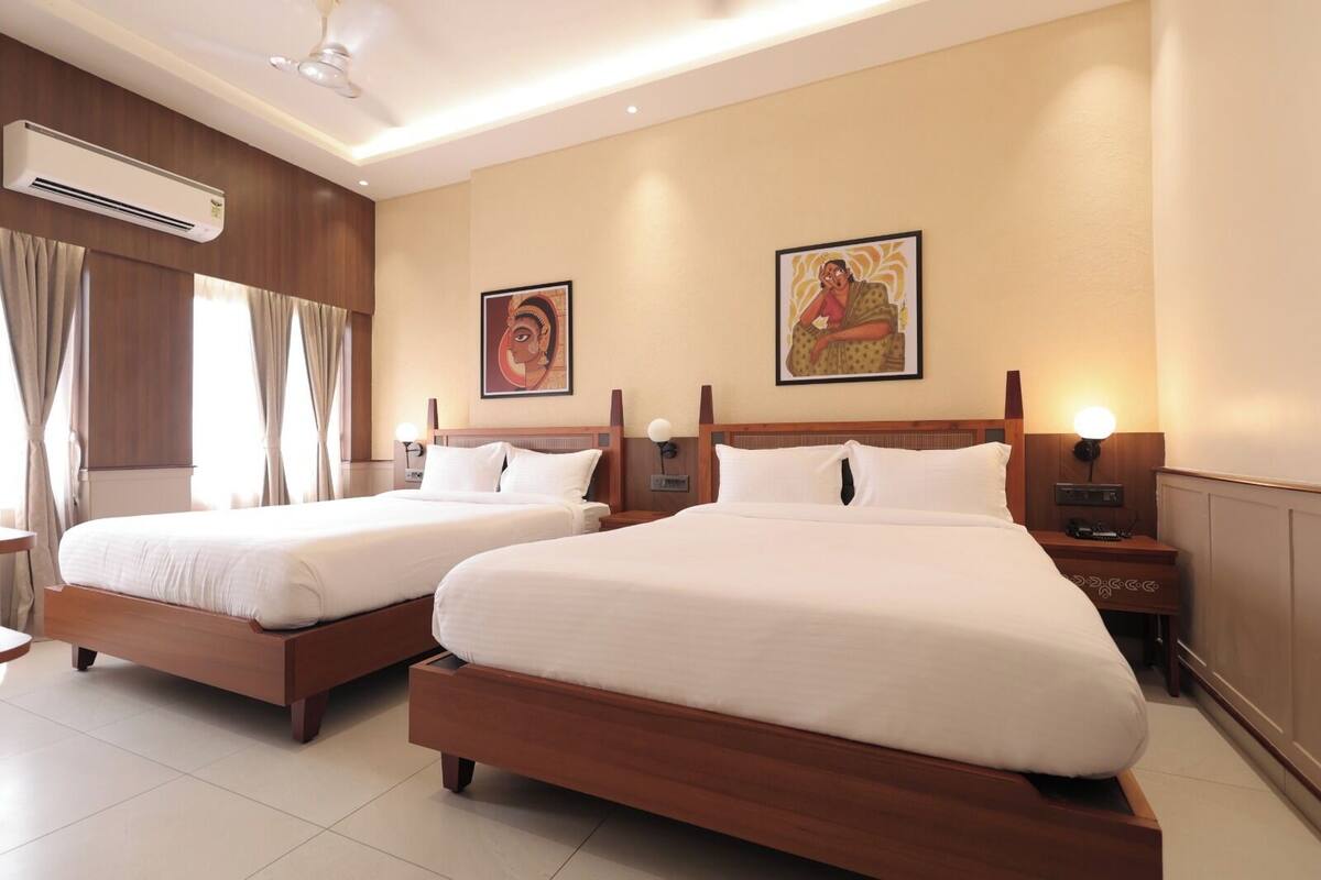 A hotel room with two wooden beds, a ceiling fan, an air conditioning unit, and two wall-mounted lamps.